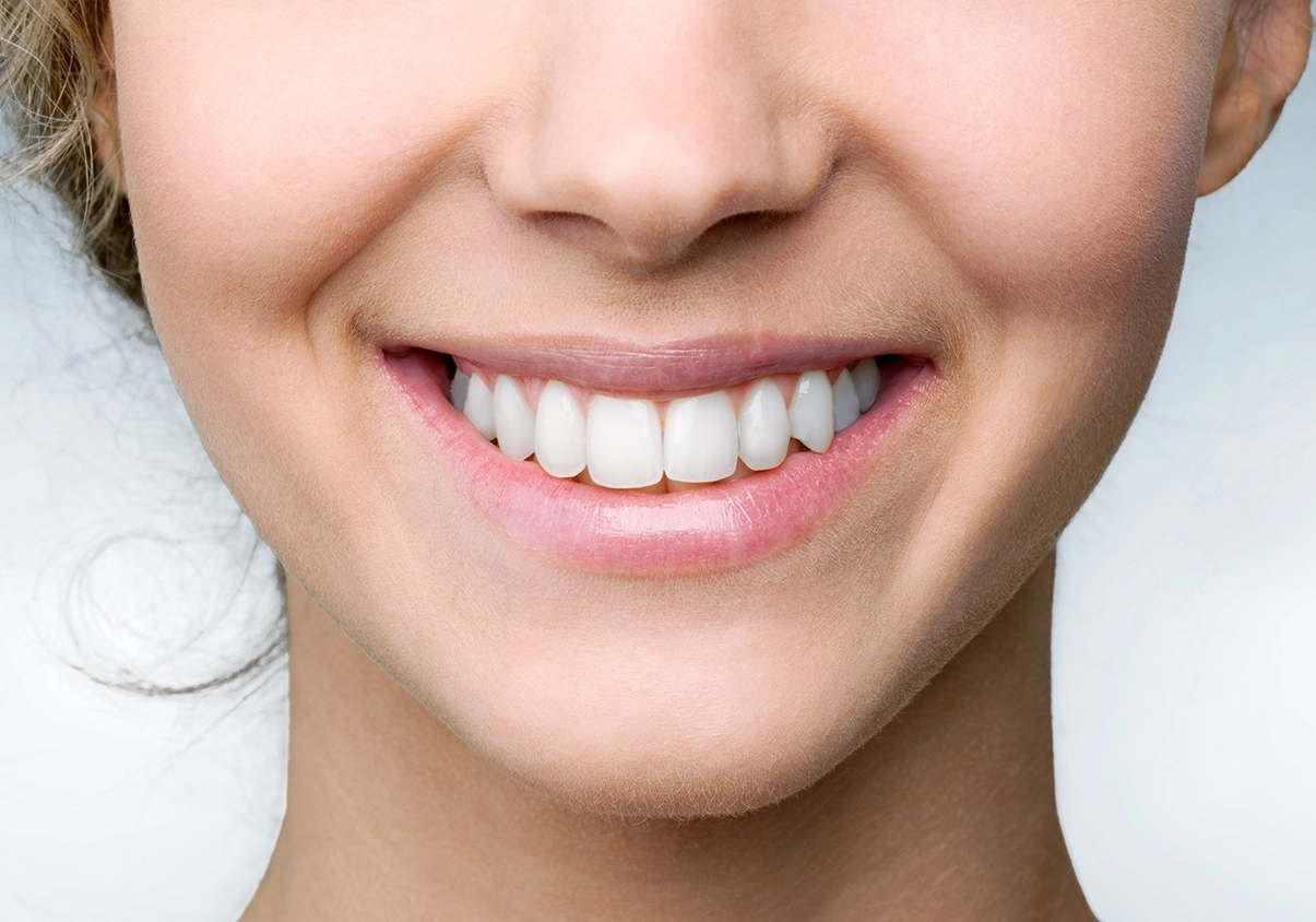 Eine Nahaufnahme des Gesichtes einer jungen Frau mit einem schönen Lächeln und gesunden weißen Zähnen zeigt.
