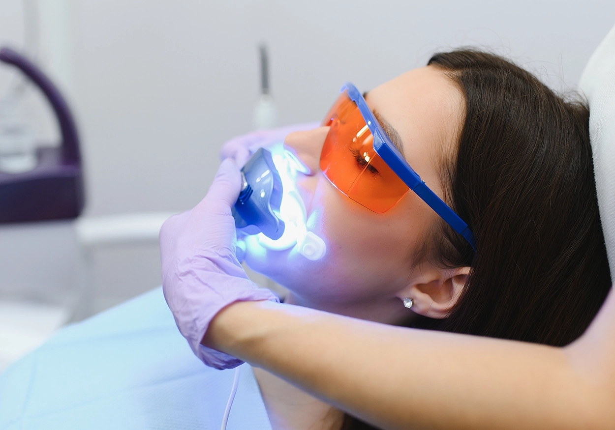 Ein Bild, das eine Frau zeigt, deren Zähne mit zahnmedizinischem Gerät erhellt werden, das von zahnmedizinischem Personal an ihren Mund gehalten wird.